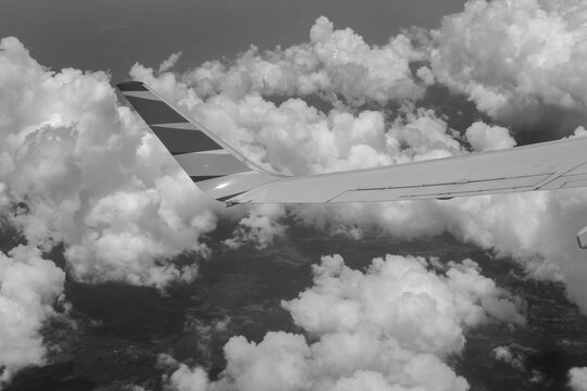 Black and white photo capturing an airplane wing above fluffy clouds, illustrating the elegance of flight and the timeless sense of freedom and wonder in high-altitude travel.