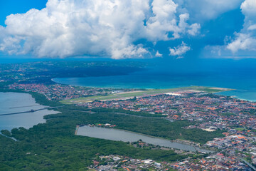 Coastal cityscape meets vibrant blue waters and lush green mangroves under dramatic clouds, showcasing the harmony between urban life and tropical nature viewed from above.