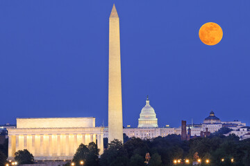 Washington DC skyline illuminated at dusk with Lincoln Memorial, Washington Monument and US Capitol, including a beautiful full orange moon on the background, USA