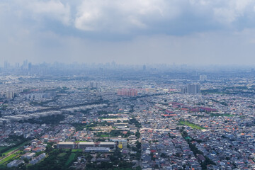 Aerial view of an urban cityscape seen from an airplane during landing, showing dense buildings, roads, and green areas under cloudy skies that create a calm metropolitan atmosphere.