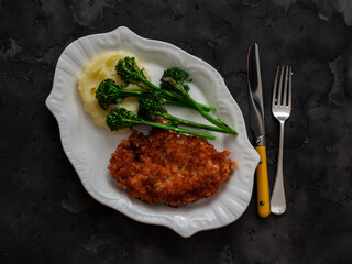 Chicken schnitzel, mashed potatoes, grilled broccoli on a dark background, top view