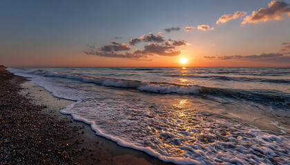 Sunset over calm ocean waves gently washing onto pebble beach under partly cloudy sky with warm light