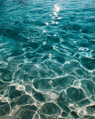 Obraz premium Clear water surface with sunlight reflections creating sparkling patterns on shallow sea floor, evoking calm and serenity