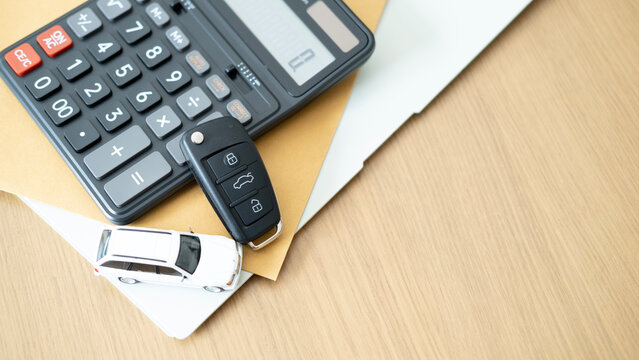Vehicle key calculator and white toy car on top of documents symbolizing auto loan insurance financial responsibility car ownership planning and economic security.