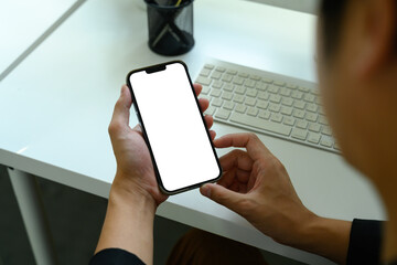 Close up of person holding smartphone with blank white screen at office desk