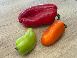 Fresh red, green, and orange bell peppers on wooden table, used in cooking, salads, and grilling, rich in vitamins and beneficial for health.