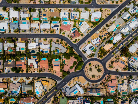 High-angle aerial shot of a large roundabout and radiating streets lined with single-family homes and palm trees in Palm Springs, California. The planned residential layout, visible swimming pools.