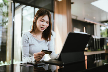 Obraz premium A young woman sitting at a desk with a laptop, holding a credit card and smiling, symbolizing online shopping and digital payment.