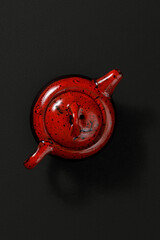 Red ceramic teapot with lid and spout, viewed from above on a dark textured background