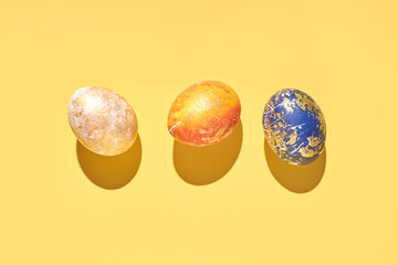 Three colorful decorative eggs on yellow background with shadows celebrating easter or spring festivities.