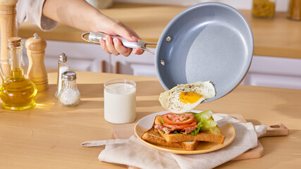 Woman Adding Fried Egg to Delicious Breakfast Sandwich in Modern Kitchen