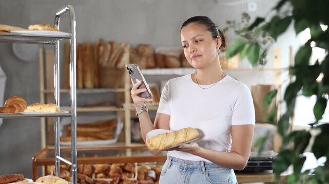  Young Asian woman checking calories of bocadillo sandwich using app and camera on phone. Woman counting calories on mobile. Woman holds a baguette sandwich in a bakery. High quality 4k footage
