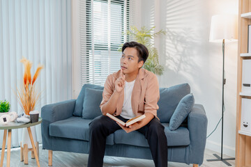 A young man sits comfortably on a sofa reading a book, appearing thoughtful and focused. The cozy indoor setting highlights relaxation, concentration, and knowledge.