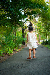 Fototapeta premium Preschool little asian girl enjoy walking on city pathway public park tree forest