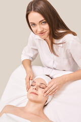 Caucasian female beautician giving relaxing facial massage to adult woman client in spa setting.