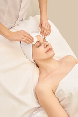 Young caucasian female receiving facial treatment in spa with gentle cleansing routine.
