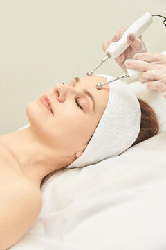 Young caucasian female receiving facial microcurrent therapy in spa setting for skin rejuvenation.