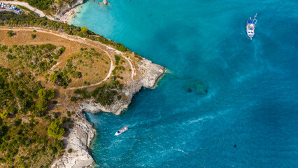 Obraz premium Zakynthos Greece aerial photo of rocky coastline with winding path green vegetation turquoise Ionian Sea and boats sailing close to the shore