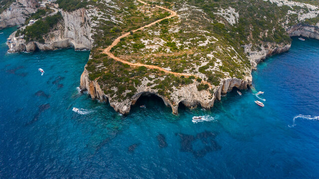Entrance to Blue Caves Zakynthos Greece aerial view with rocky cliffs turquoise Ionian Sea boats sailing near cave openings and winding cliff path - Powered by Adobe