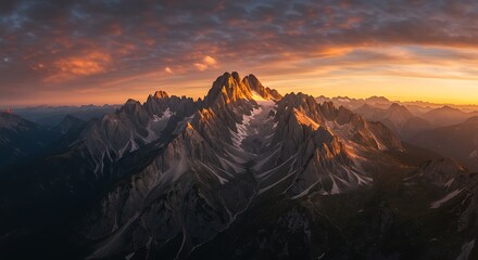 Sunset over a rugged mountain range with snow-capped peaks and dramatic lighting