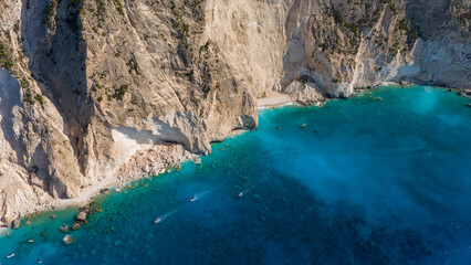 Aerial view of steep limestone cliffs with narrow sandy beach turquoise Ionian Sea clear shallow water and dramatic coastline in bright sunlight
