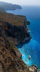 Aerial view of Plakaki coast with steep rocky cliffs turquoise Ionian Sea and dry burned grass covering the rugged hillside above the shoreline