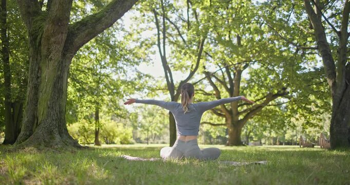 young beautiful white girl doing yoga in park among trees in clearing on summer day