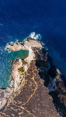 Top view of Plakaki beach Zakynthos Greece rocky peninsula meeting turquoise shallows and dark blue Ionian Sea with steep barren cliffs inland