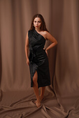 Full length portrait of pretty young barefoot brunette woman in black dress on brown background