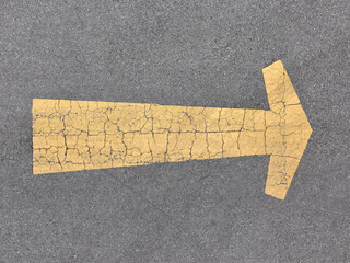 cracked yellow arrow road marking on asphalt surface, worn direction arrow texture