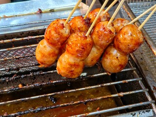 Several skewers of small, round Thai sour sausage (Sai Krok Isan) being grilled over a hot metal grate. 