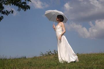 girl in a white dress in a blue green meadow with an umbrella