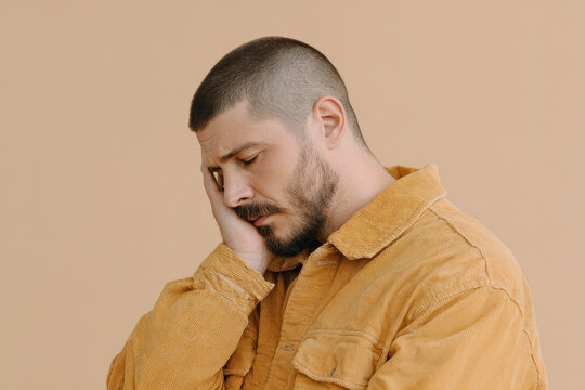 man with his hand on his face and tense jaw expresses deep contemplation against clean solid background