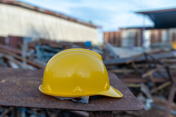 Safety First: A yellow safety helmet rests on a metal surface in a construction site, with industrial buildings in the background, depicting a scene of preparedness and responsibility.