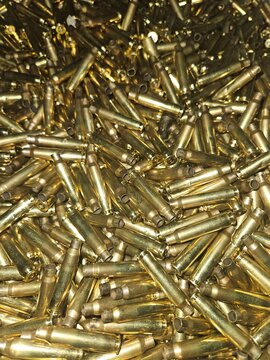 A pile of spent rifle brass bullet casings, gleaming under a bright light, ready for reloading or recycling.