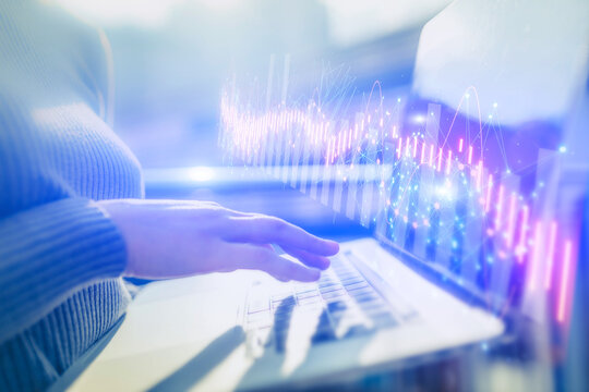A woman is typing on a laptop computer, stock trading graphs