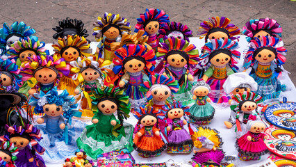 A table is filled with a variety of dolls, each with unique outfits and accessories. Historic...