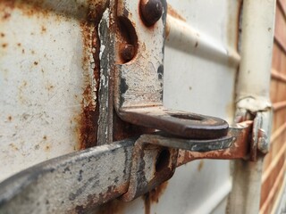 Close-up of a rusty metal latch on a weathered door with peeling paint and bolts. Ideal for industrial, decay, texture, or aging themes in design and documentation