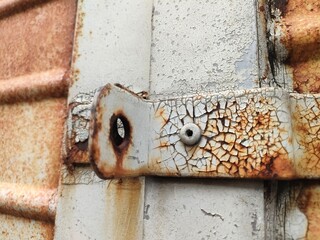 Close-up of a rusty metal latch on a weathered door with peeling paint and bolts. Ideal for industrial, decay, texture, or aging themes in design and documentation