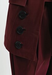 Close-up of a dark burgundy tailored suit showcasing a detail of three vertically aligned black buttons on the sleeve.  The fabric appears smooth and possibly slightly shiny