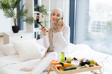 Young Muslim woman wearing hijab records skincare tips using avocado in bright modern room