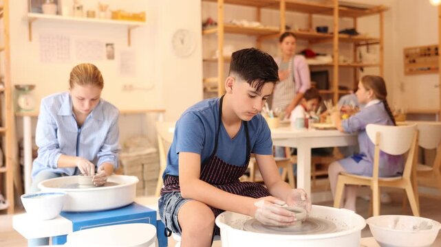 Pleased underage attendees of pottery circle working at throwing-wheel with female instructor