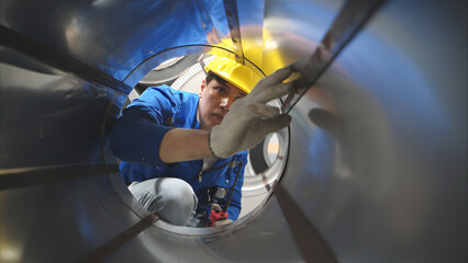 Industrial worker inspecting inside a large metal tube in a factory