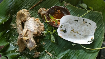 Remnants of a traditional Indonesian meal with chicken bones, herbs, and empty bowls on banana leaf. Ideal for culinary, culture, food waste, or street food-themed visual content