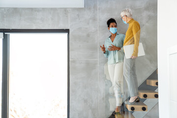 Businesswomen wearing masks collaborating in modern office, teamwork with laptop