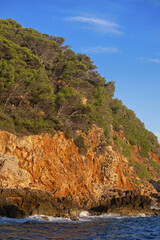 striking coastal landscape with reddish-brown cliffs rising steeply from the deep blue sea. The cliffs are topped with green vegetation,in Bandol,  France