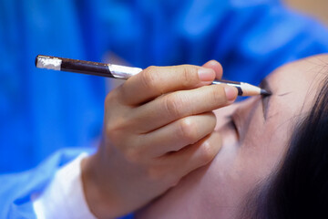 The tattoo artist is drawing the eyebrows of a customer.