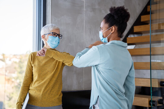 Businesswomen wearing masks collaborating in modern office, teamwork with laptop - Powered by Adobe