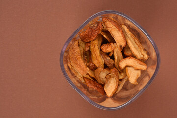 An abstract view of a pile of brown dried apples in a square plastic bowl on a brown background