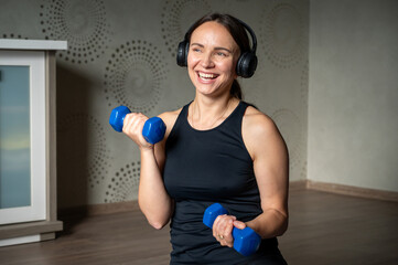 Smiling woman training with dumbbells at home wearing headphones